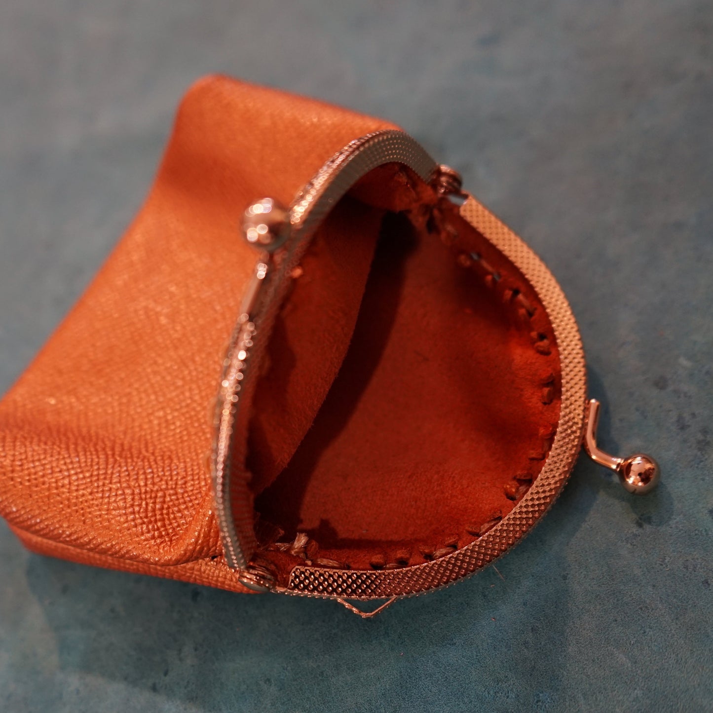 Small orange fabric pouch with a metallic clasp on a textured gray surface