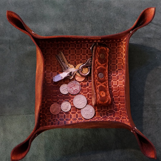 Brown leather tray with keys and coins on a dark gray background