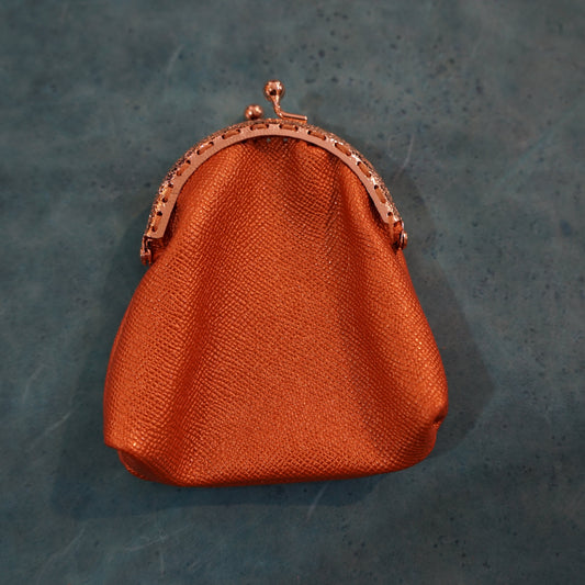 Orange textured handbag with a bronze clasp on a dark gray background