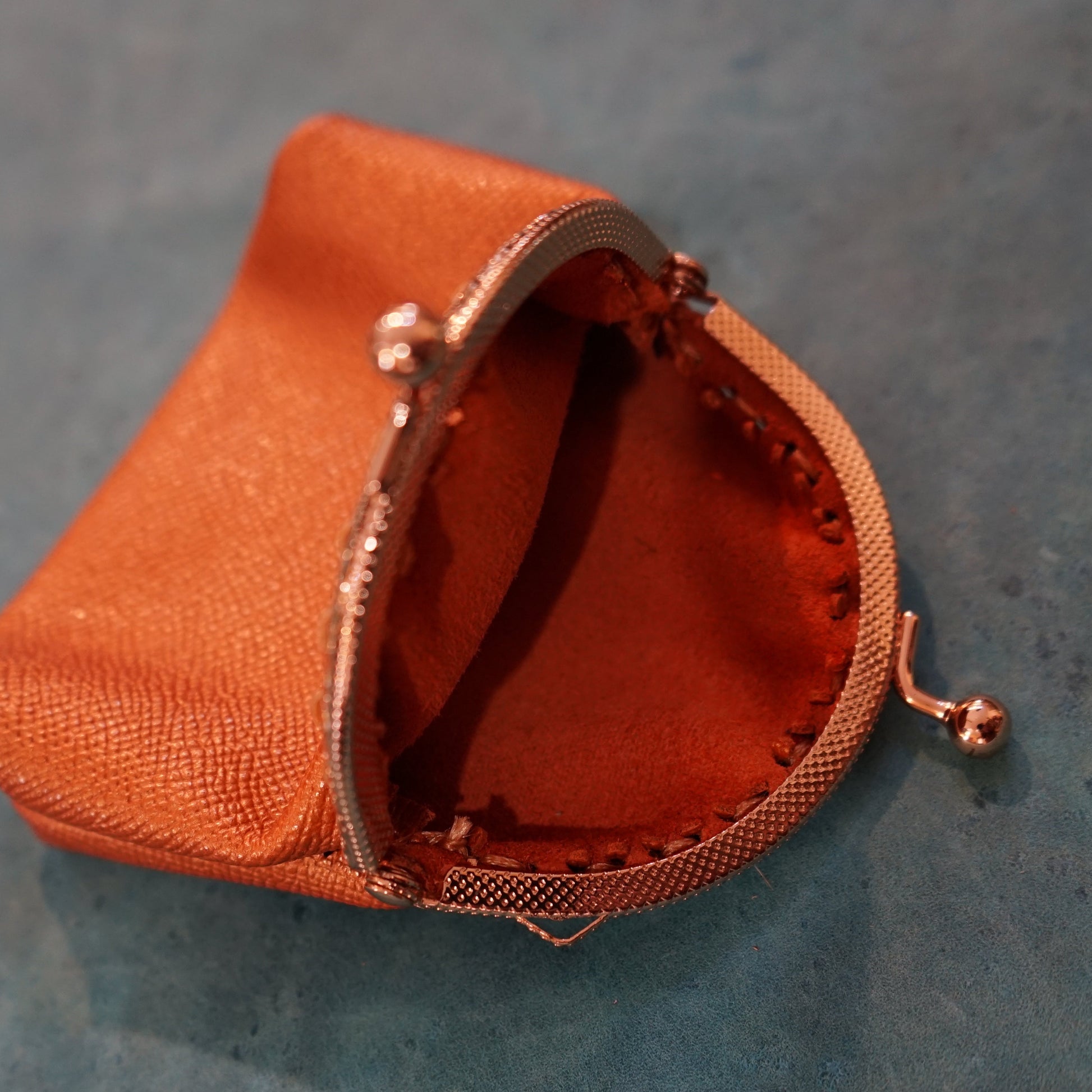 Small orange fabric pouch with a metallic clasp on a textured gray surface