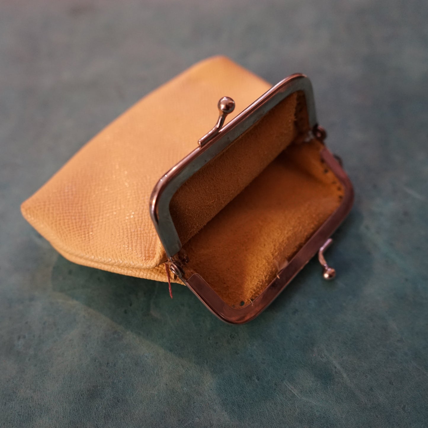 Small tan leather purse with a bronze clasp on a textured green surface